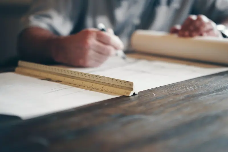 A drafter working on architectural plans with a pencil and ruler
